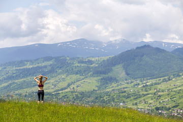 Fototapeta na wymiar Slim young woman with raised arms outdoors on background of beautiful mountain landscape on sunny summer day.
