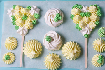 Marshmallow in the form of a heart on a stick. Made from different color elements. Next to it is marshmallows of various shapes and colors. Shot from above.