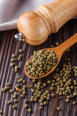 green peppercorns in wooden scoop on rustic background