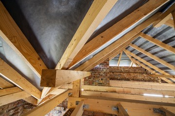 Attic of a building under construction with wooden beams of a roof structure and brick walls.