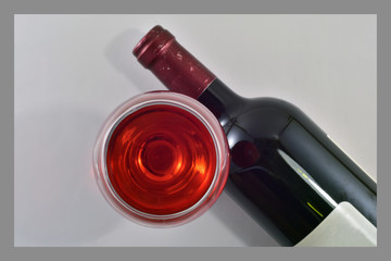 Bottle and glass of red wine on a gray background with a fringing