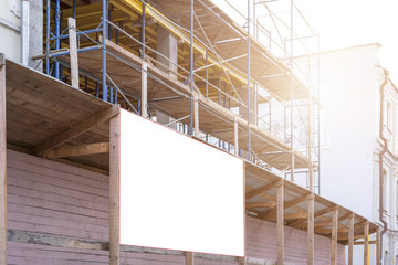 large blank mock-up billboard hangs on construction scaffold in street at sunlight