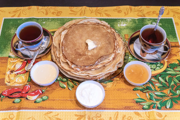 On the table, tea with pancakes, sour cream and jam for the Maslenitsa holiday, which is celebrated in Russia at the end of winter.
