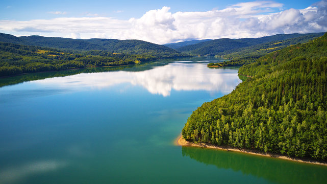 Reflection of sky, clouds, forest and mountains in water. Summer landscape with lake and mountain woodland