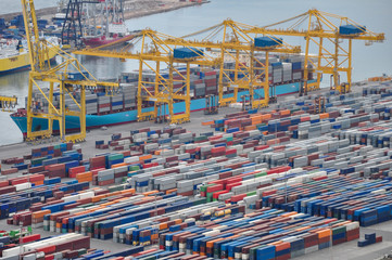 container ship clears and loads freight in the port of Barcelona with many stacked containers in the foreground