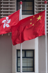 close shot of the flag of the People's Republic of China in front of the flag of Hong Kong with a symmetrical building wall in the background