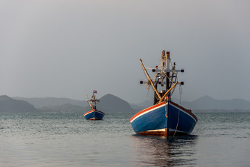 two small Thai fisherman boats in the Thai national colours red, white and blue anchoring in the sea with some mountains in the distant background