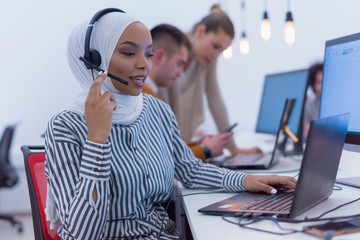 Female Customer Service Representative Answer Client's Questions in a Headset. Multi-Ethnic Team of Specialists. Happy african muslim woman in call center.