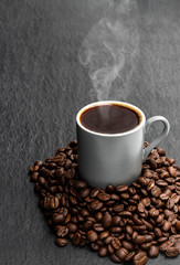 Black coffee in small cup with beans on black stone background