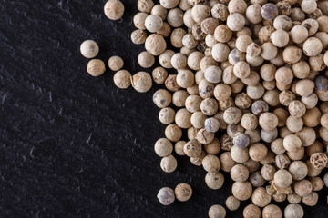 white peppercorns on dark slate stone background