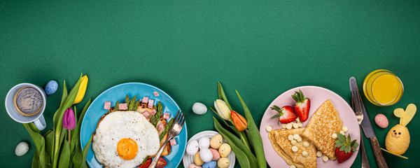 Easter breakfast flat lay with scrambled eggs bagels, tulips, pancakes, bread toast with fried egg and green asparagus, colored quail eggs. Top view. Copy space. Banner.