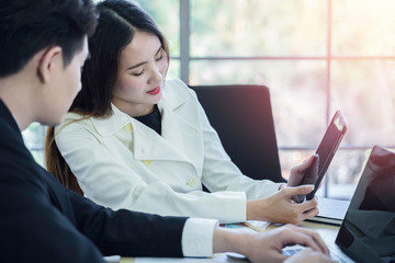 Two young Asian business colleagues using tablet at meeting in modern office. Smart coworkers discuss and brainstorm for new project planning together. Communication and business concept, Daylight.