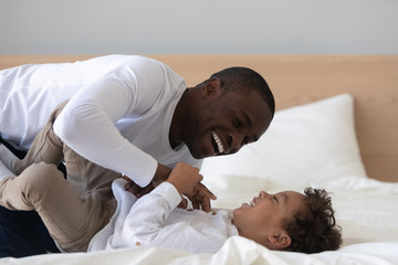 Happy African American father tickling laughing adorable son in bed