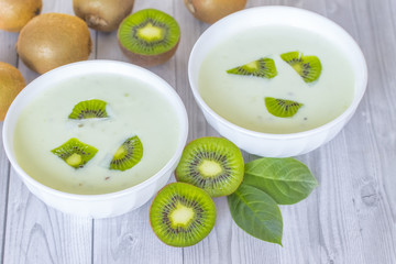 kiwis lie on the table next to bowls of fruit yogurt with kiwi slices. healthy yogurt in bowls with kiwi slices and kiwi halves and whole kiwi fruit on the table close-up. background with yogurt and k