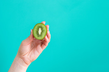 woman hand holding kiwi fruit half on green background copy space - obrazy, fototapety, plakaty