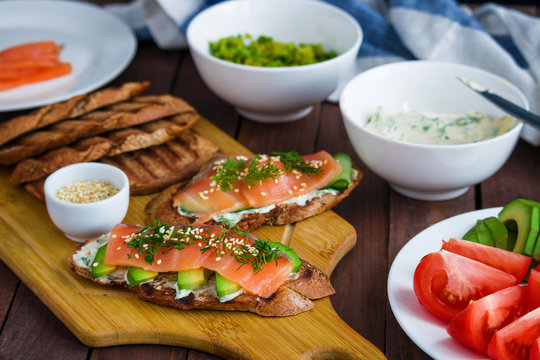 healthy sandwiches toats with salmon avocado cucumber  cream cheese dill on cutting board and other ingredients