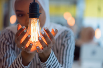 Beautiful african muslim woman holds modern lamp bulb with smiling happy expression, idea concept...