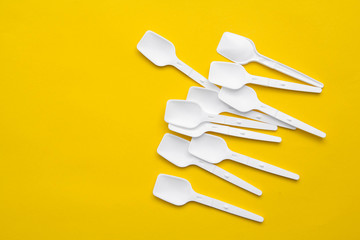White plastic spoons on yellow background. Fast food, eco and no plastic concept. Top view. Copy, empty space for text