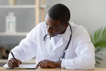 Serious African American doctor filling patient form document close up