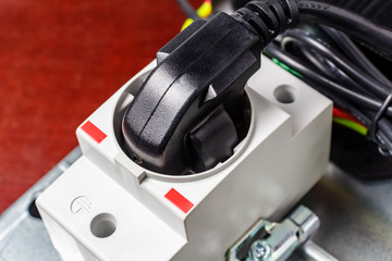 Black and shiny power plug inserted to the white electrical socket on DIN rail close-up. DIN rail electrical equipment