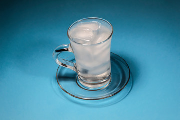 Against a blue background is a cup in which is clear water and ice.