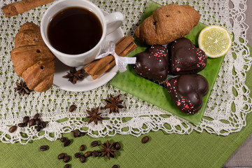 On a white saucer is a cup of coffee, cinnamon sticks and a croissant. On a green saucer lies cookies, croissant and lemon.