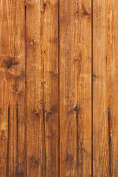 Background of old unpainted wooden slats planks stacked vertically. The color is dark yellow, red, brown. Stain and varnish coating with drips of rust from nails. Natural wood backdrop