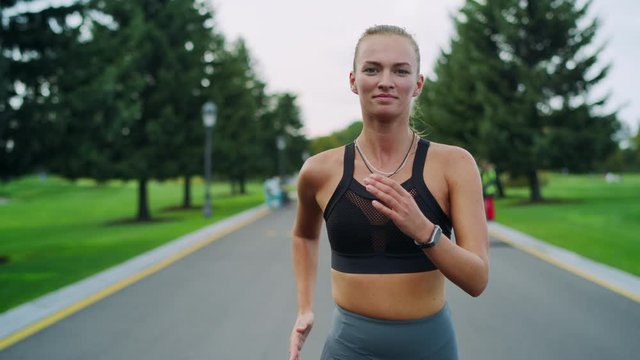 Happy athletic woman jogging in park. Girl doing cardio workout outdoors