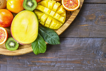 kiwis, oranges and mangoes on a wooden background top view. fruit background. halves of fruit and whole fruits of mango, kiwi, oranges in a wooden bowl top view. copy of the space.