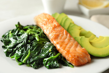 Tasty salmon with spinach and avocado on plate, closeup