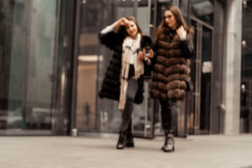 Female friendship, relationships. Two girls are drinking coffee on the street near glass office buildings, a corporation, a bank. The end of the working day of the manager. Coffee on the run.