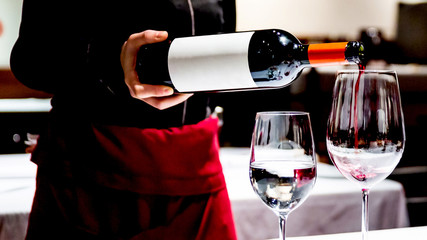 Crop image of Sommelier pouring perfect red wine in a wine glass for celebrating a special...