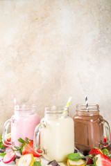 Three mason jars with milkshakes or smoothie. Summer healthy breakfast, lunch drinks - banana, chocolate and strawberry milkshakes on wooden background