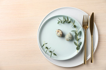 Festive Easter table setting with quail eggs on wooden background, flat lay.