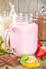 Three mason jars with milkshakes or smoothie. Summer healthy breakfast, lunch drinks - banana, chocolate and strawberry milkshakes on wooden background