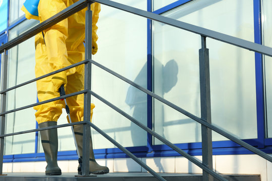 Male worker in protective suit spraying insecticide on stairs outdoors, closeup. Pest control