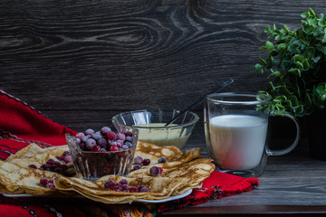 Maslenitsa: thin pancakes with berries and a glass of milk on a wooden table.