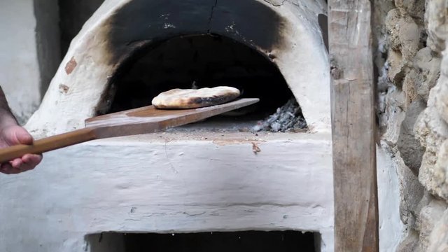 The Baker took the baked flatbread out of the oven with a wooden spatula