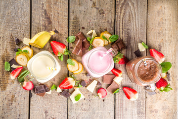 Three mason jars with milkshakes or smoothie. Summer healthy breakfast, lunch drinks - banana, chocolate and strawberry milkshakes on wooden background