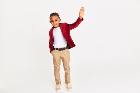 Body language, signs and symbols concept. Full length shot of confident handsome African schoolboy in stylish clothes raising hand, waiving, making greeting gesture, saying Hello, drawing attention
