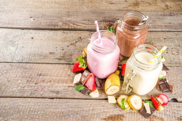 Three mason jars with milkshakes or smoothie. Summer healthy breakfast, lunch drinks - banana, chocolate and strawberry milkshakes on wooden background