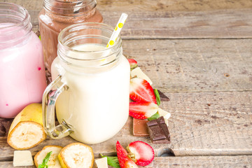 Three mason jars with milkshakes or smoothie. Summer healthy breakfast, lunch drinks - banana, chocolate and strawberry milkshakes on wooden background