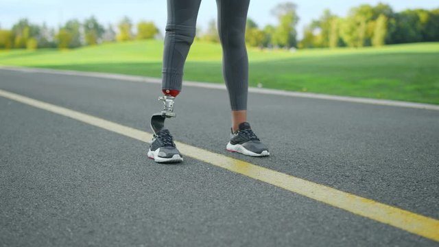 Woman with prosthetic leg standing on road.Athlete legs preparing to run in park