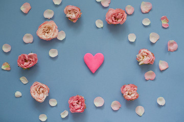 Bright pink heart inside frame of roses and petals on a blue background