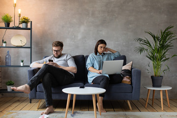 A young Couple on the Couch are Passionate about Gadgets. Small Children Play Around Their Parents. Social Photo.