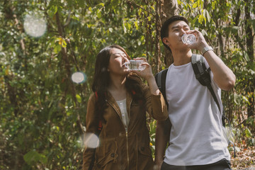 Naklejka premium Asian young couple hiking in the forest have a break and drinking water. Travel and adventure concept.