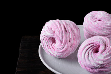 Berry zephyr topped with sugar powder on the ceramic plate against the black background