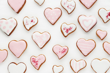 Obraz premium pattern of gingerbread cookies in the shape of a heart decorated with white and pink glaze on a white wooden background..