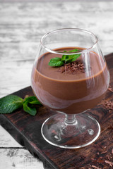 Chocolate pudding topped with mint in the glass on the white wooden table