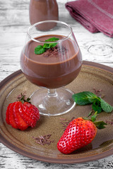 Chocolate pudding topped with mint in the glass. Ripe strawberry on the ceramic plate on the white wooden table